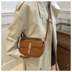Detailed close-up of brown saddle bag with gold metal buckle on a beige trench coat