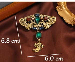 Macro view of vintage gold brooch with emerald green stone and cupid pendant detail