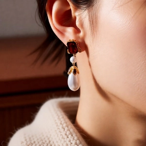 Detail of vintage gold pearl drop earring with red gemstone on model side view