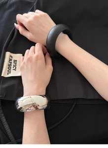 Close-up of a high-gloss silver metal bangle and matte black bracelet on a model wrist