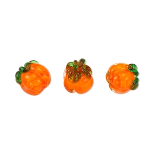 Three orange glass pumpkin beads with green leaves on white background for DIY jewelry