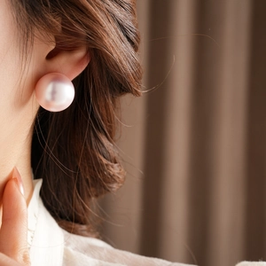 Close-up of a large pink pearl stud earring with natural luster on a female model