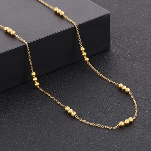 Close-up of golden beaded link chain necklace featuring groups of three small gold beads