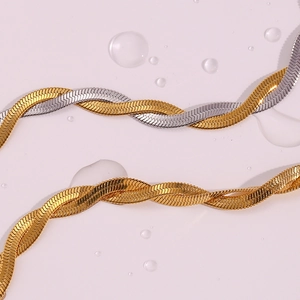 Detail of two-tone and gold woven flat herringbone anklets on a wet pink surface
