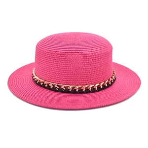 Détail d'un chapeau de paille rose avec ruban en cuir noir et chaîne dorée élégante