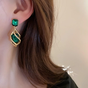 Vintage geometric emerald drop earrings with gold spiral cages on a female model