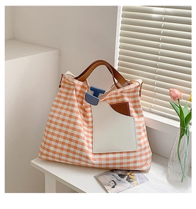 Orange checkered canvas tote bag with brown straps and blue clasp on a sunlit table