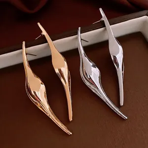 Minimalist fluid curved earrings in gold and silver finish on a brown leather base