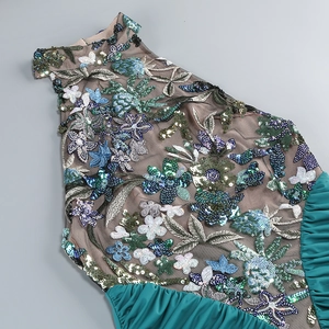Close-up of floral embroidery and sequins on sheer mesh with emerald green pleated fabric