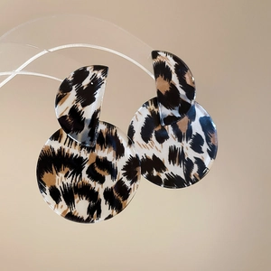 Macro shot of geometric acrylic leopard print drop earrings on a minimalist stand
