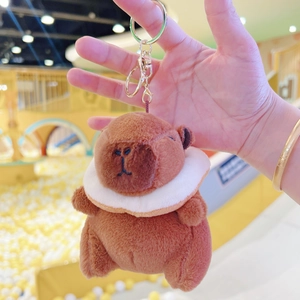Cute brown plush capybara keychain with white collar and gold ring on blurred background
