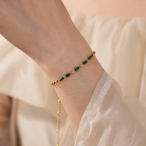 Gros plan d'un bracelet vintage en acier inoxydable avec billes dorées et pierres vertes