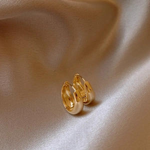 Gros plan de boucles d'oreilles créoles dorées en U sur un tissu en soie champagne