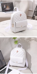 Detail of white quilted backpack with gold rose emblem on front pocket and marble background