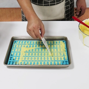 Spreading batter into bone-shaped silicone mold with a white scraper on a baking sheet