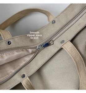 Detailed macro shot of the metal zipper and canvas texture on this tote bag