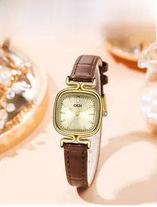 Detail of square gold watch face with sunray texture and brown leather strap