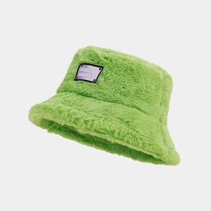 Détail d'un bob en peluche verte avec écusson brodé violet 'MAKE IT HAPPEN' sur le devant