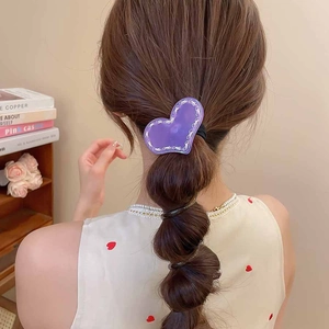 Détail d'un chouchou cœur en acrylique violet sur une coiffure tressée