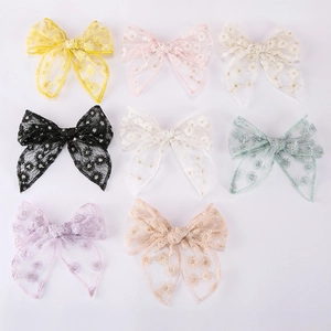 Flat lay of eight embroidered floral bow hair clips in various pastel colors on white