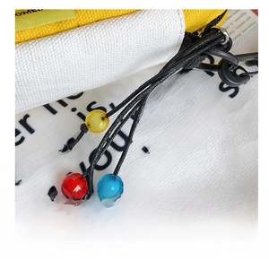 Close-up of yellow and white canvas bag with colorful faceted beads on black strap