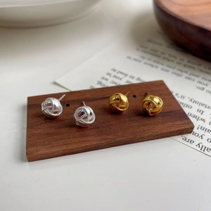 Detalle de pendientes de nudo de plata S925 en oro y plata sobre un soporte de madera