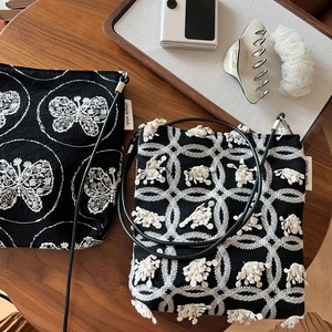 Close-up of black canvas bag with intricate white butterfly embroidery and leather strap