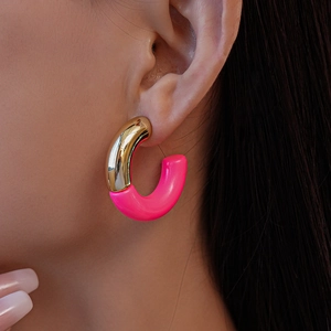 Close-up of a C-shaped earring in gold metal and bright pink resin on a model ear
