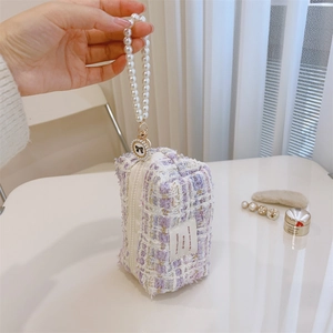 Detail of tweed vanity bag featuring a pearl bead handle and decorative bow pendant