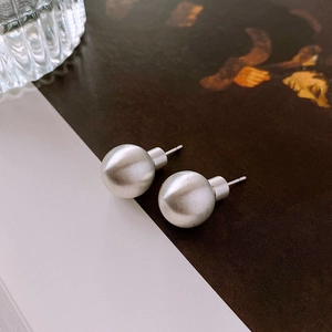 Macro shot of silver ball stud earrings with matte brushed texture on artistic background