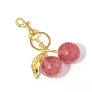 Macro shot of pink glitter resin cherry keychain with golden lobster clasp and leaf