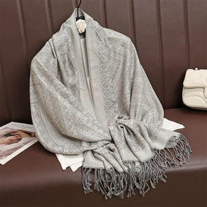 Dettaglio macro di sciarpa jacquard grigia paisley con nappe su divano in pelle