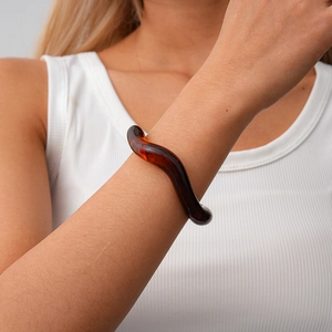 Close-up of model wearing deep amber wavy acrylic cuff with irregular geometric design
