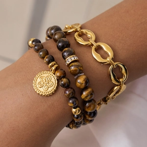 Close-up of stacked tiger eye bead bracelets and a gold link chain on a woman's wrist