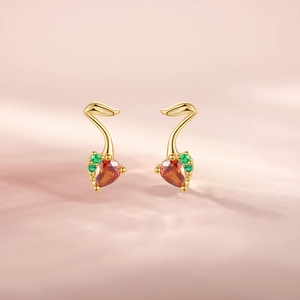 Detailed macro of golden heart-shaped orange gem earrings with green leaf accent gems