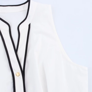 Detailopname van een witte mouwloze top met zwarte contrastbies en een gouden knoop