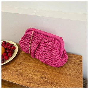 Close-up of woven fuchsia clutch bag with gold chain strap on a wooden table