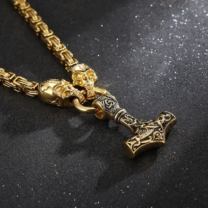 Detailed close-up of golden Viking Mjolnir pendant with ornate skull connectors and chain