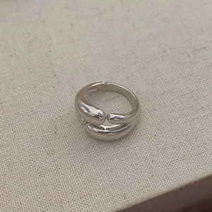 Macro detail of silver double-layered ring with organic fluid shape on beige linen