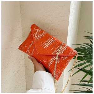 Detail view of orange crocodile pattern envelope bag with a thin gold chain strap