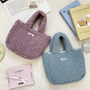 Top view of two soft faux shearling tote bags in purple and blue with brand labels