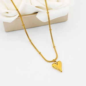 Detail of a gold snake chain necklace with beads and a 3D heart pendant on a gift box