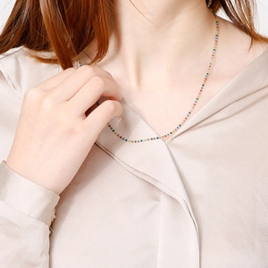 Dettaglio di una collana girocollo di perline colorate su una modella in seta beige