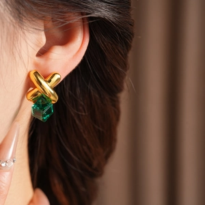 Close-up of vintage gold crisscross earring with a green cube crystal pendant on a model