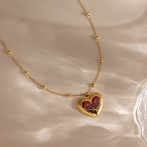 Collier doré avec pendentif cœur orné de zircons rouges sur une chaîne perlée