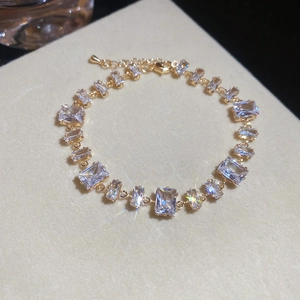 Detailansicht eines goldenen Zirkonia-Armbands mit funkelnden Kristallen auf beigem Kissen.