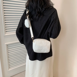 Close-up of white heart-embossed crossbody bag with wide strap and round coin purse