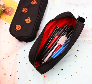 Close-up of black canvas pencil case with orange bear embroidery and red inner lining