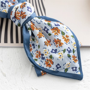 Close-up of blue floral satin fabric bow clip with orange flowers and green leaves detail