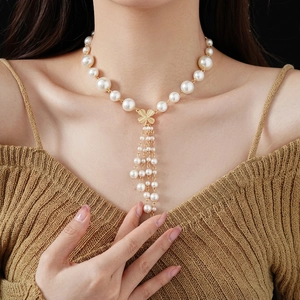 Faux pearl tassel necklace with golden clover pendant on elegant brown knit sweater